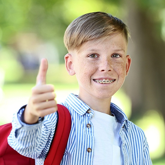 Young boy with braces smiling and giving thumbs up